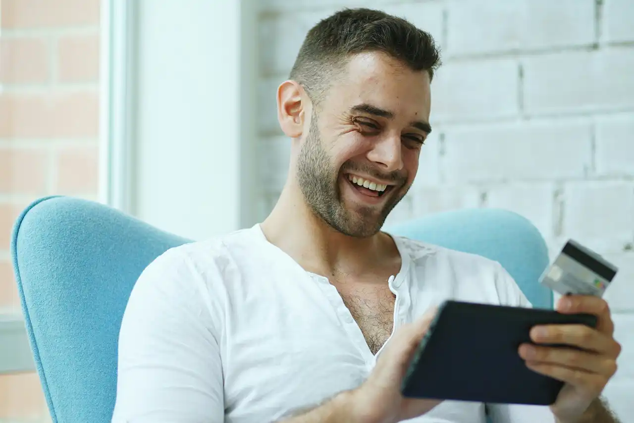 Mann mit Kreditkarte und Tablet sitzt auf einem Sofa.