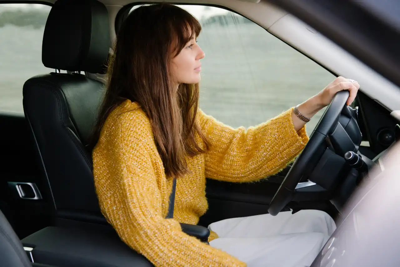 Une femme au pull jaune conduit une voiture