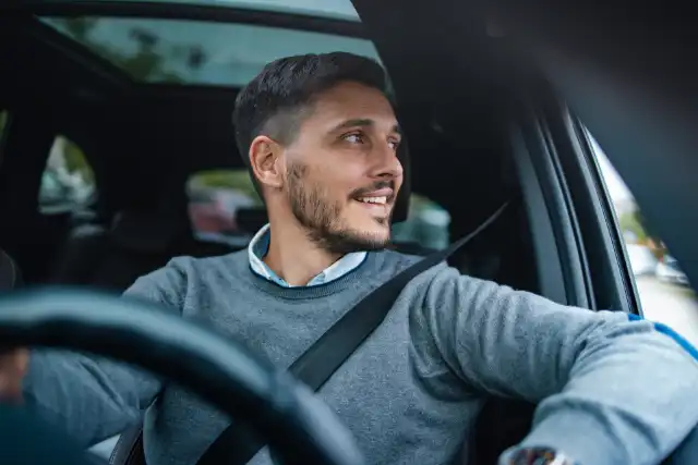 Un uomo con un maglione grigio guida un'auto