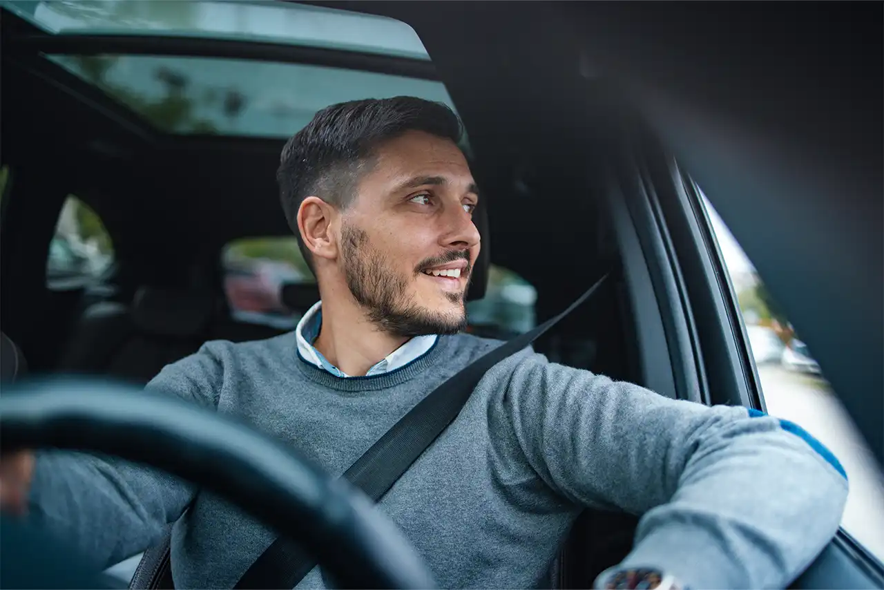 Un uomo con un maglione grigio guida un'auto