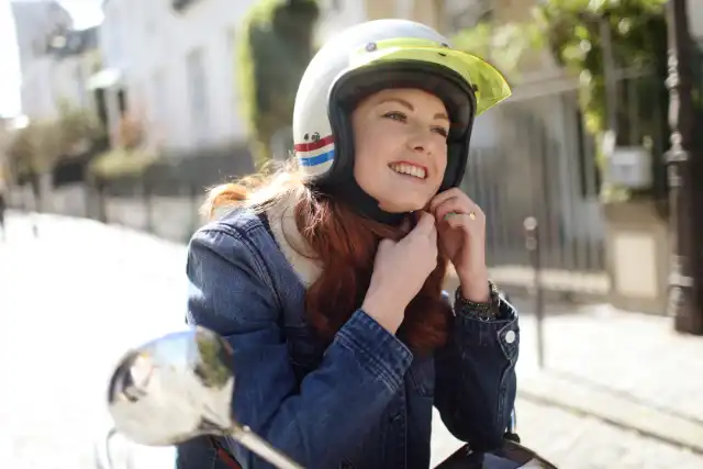 A woman wears a helmet and rides a scooter