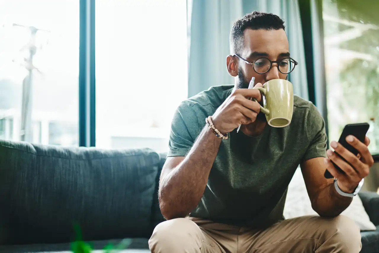 Man drinks from a cup and sits on the sofa